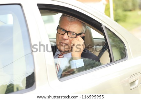 Senior businessman working in back of car and talking on his mobile phone