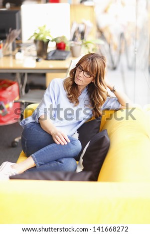 Female executive art director relaxing on couch at lunchtime in advertising agency. Shallow focus.