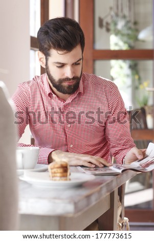 Young man sitting at table and reading newspaper in coffee shop.