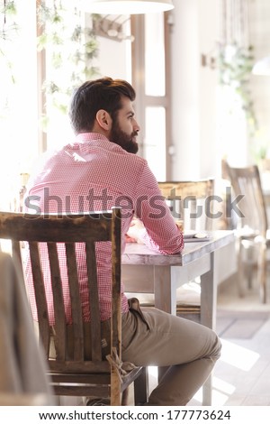 Modern young man sitting at table in coffee shop.