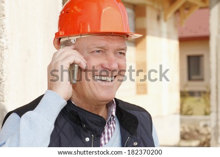 Close-up portrait of smiling senior construction architect while using mobile phone
