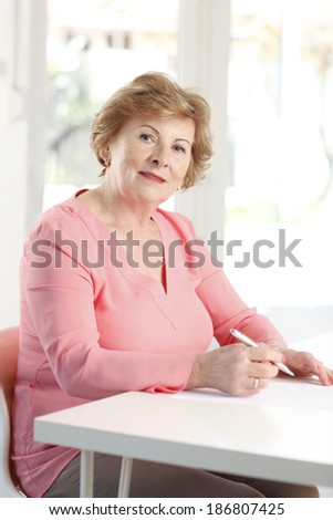 Portrait of senior woman sitting at desk and writing.