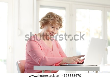 Portrait of senior woman sitting at desk and working on laptop.