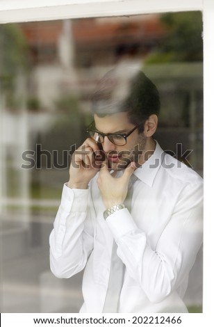 Executive young businessman standing behind window while using his handy. Small Business.