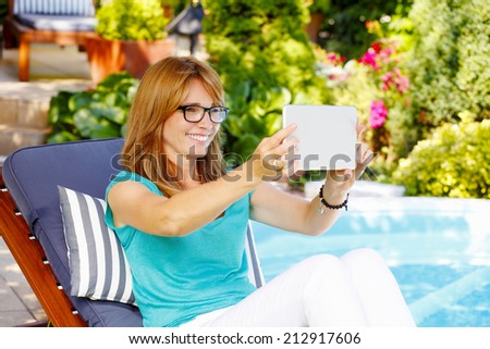 Portrait of attractive middle age lady sitting at garden while taking selfie.