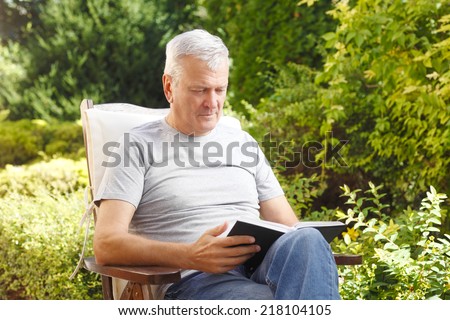 Grandfather sitting at garden, while reading book.