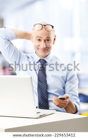 Portrait of middle age sales man holding mobile, while working at office.