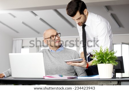 Senior businessman giving advise to young colleague while they working on laptop and digital tablet at office.