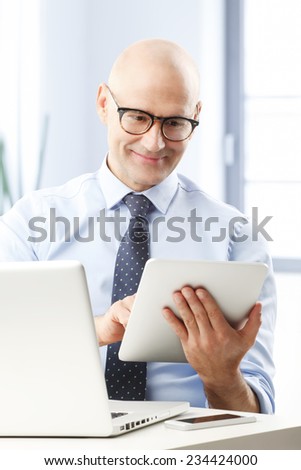 Executive financial businessman holding digital tablet while sitting at office and working on financial plan.