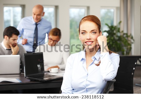 Portrait of executive sales woman sitting at office, while business people working at background. Teamwork.