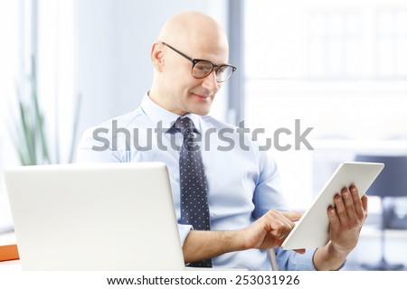 Portrait of executive business man sitting at desk and touching digital tablet.