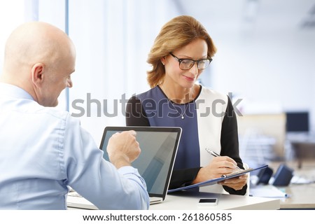 Executive business woman using clipboard while sitting at office and consulting together with colleague.