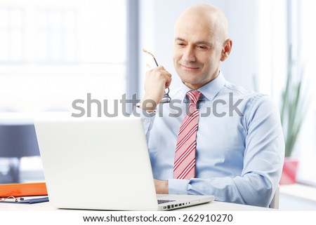 Portrait of sales man sitting at office while reading business report on laptop.
