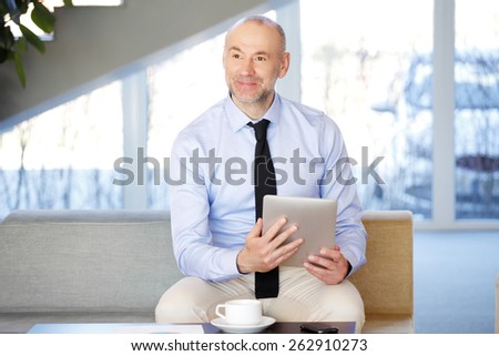 Busy businessman sitting on sofa at office while holding hands digital tablet.