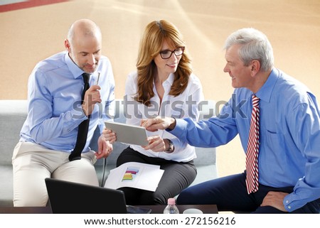 Image of middle age businesswoman holding digital tablet while sitting at office with businessmen and consulting from financial plan. Sales team at work.