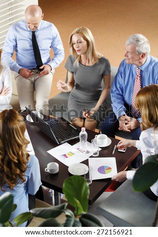 High angle view of financial business people sitting at meeting. Businesswomen and businessmen sitting at desk in front of computer and consulting from financial investment. Teamwork at office.