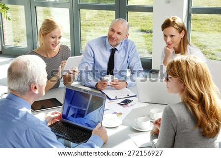 Group of business people sitting at office.  Businesswomen and businessman consulting with each other and working on new plan while sitting around the conference table and using laptop and tablet.
