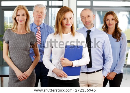 Successful group of business people portrait. Image of executive business woman holding file in her hand and standing at office with her business team.