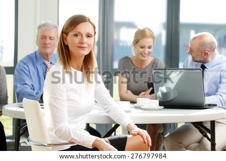 Executive businesswoman portrait. Image of mature sales woman sitting at office while business team consulting at background.