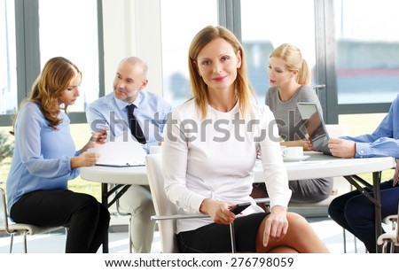 Executive businesswoman portrait. Image of of mature sales woman sitting at office while business team consulting at background.