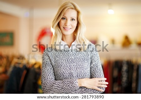Close-up portrait of clothing store owner with arms crossed standing in her shop while looking at camera and smiling. Small business.