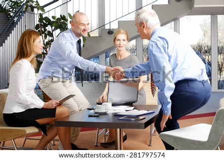 Image of business team sitting at meeting while two businessmen shaking hands. Teamwork at office.