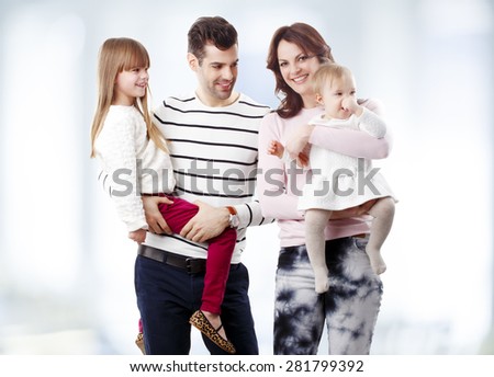 Image of young family standing at living room. Mother holding her baby girls while young father lifting daughter.