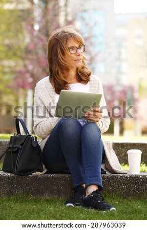 Portrait of casual businesswoman sitting at park and using digital tablet. Middle age woman working online.