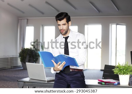 Portrait of casual young sales assistant standing at office in front of desk while holding hands business document.