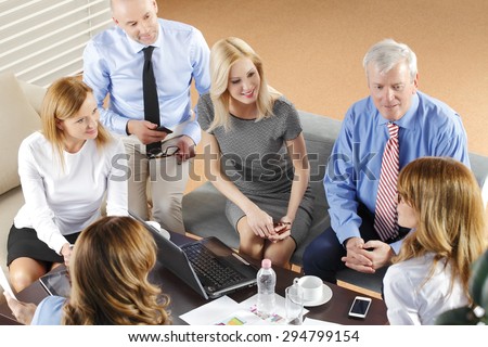 High angle view of business team in a meeting. Businesswomen and businessmen sitting around conference table and working with laptop and digital tablet while consulting.