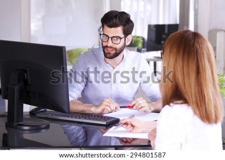 Portrait of young businessman sitting with sales woman in front of personal computer and consulting. Executive businesswoman giving advise to young professional. Teamwork at office.