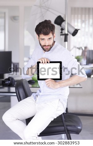 Portrait of young photographer sitting at his studio. Professional man holding hands digital tablet with empty screen.