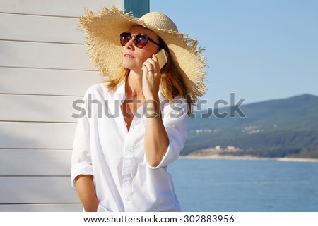 Close-up portrait of smiling female by the sea. Happy woman standing at the seaside and making call.