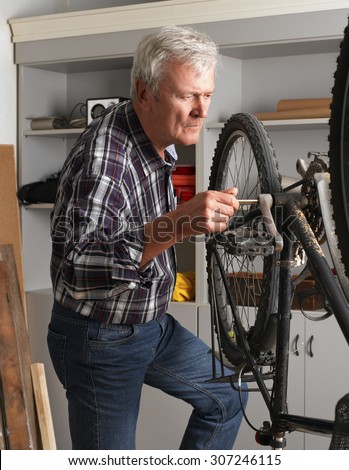 Portrait of retired man standing next to bike and working at his workshop. Small business.