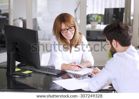 Portrait of mature insurance agent giving advise her new client while sitting at office in front of computer. Businesswoman making financial plan.