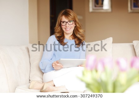 Portrait of casual businesswoman. Middle age professional sitting at home and working online while looking at camera and smiling.