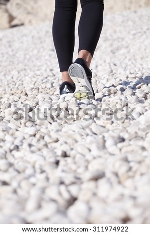 Close-up portrait of a women\'s running shoe in use. Sporty woman walking on the beach after morning run.