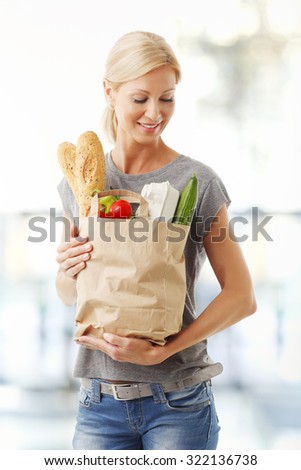 Portrait of middle age woman holding in her hand a paper shopping bag full of foods while standing at food market.