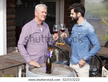 Portrait of young and senior man tasting with red wine in a vineyard. Professional winemakers standing in front of wine cellar and consulting. Small business.