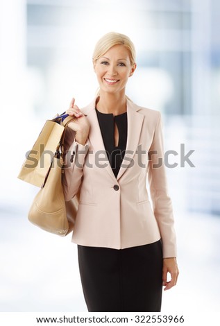Portrait of beautiful woman holding in her hand a paper shopping bag and a handbag while standing at store.