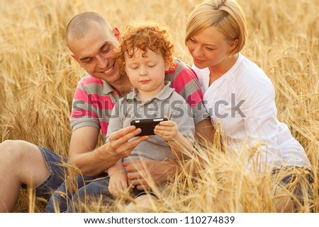 happy family having fun in the wheat field. Father and mother behind their son. Son watching something in dad\'s mobile (cell) phone. outdoor shot