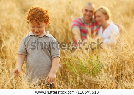 happy family having fun in the wheat field. Father and mother hug each other behind their son. Son whatching wheat. outdoor shot