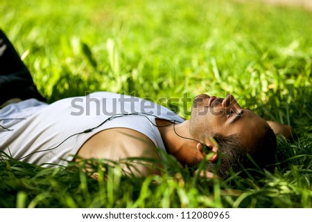 Portrait of a relaxed young male listening to music on headphone while lying in a park - Outdoor
