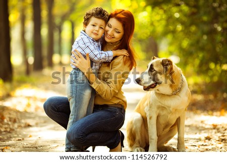 happy mother playing with her son in the park and dog sitting and watching