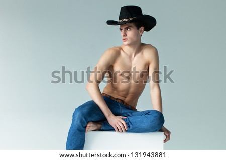 Portrait of a well built shirtless muscular male model in cowboy hat sitting on the cube