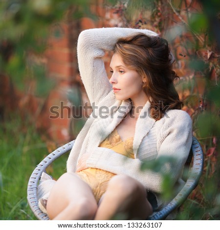 Fashion portrait of young sensual woman in garden  sitting in the chair