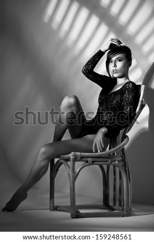 artistic portrait of fashion woman sitting on the chair with shadows on the wall behind her, black and white