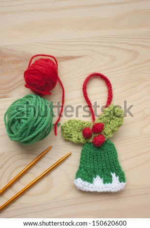Traditional hand crafted Christmas tree ornament knitted festive bell and golden knitting needles. Red and green wool used for knitting.