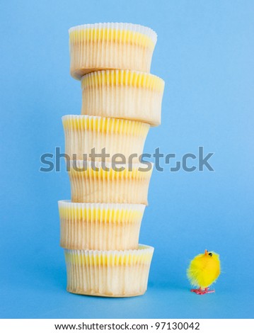 Yellow cute chick looking up to the top of a huge lemon cupcake tower. Fluffy chick and lemon cupcake tower. Comical Easter image concept.