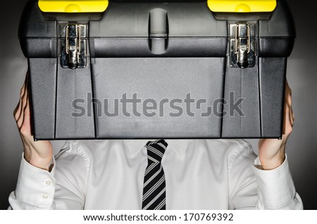 Man wearing tie holding toolbox in front of his face